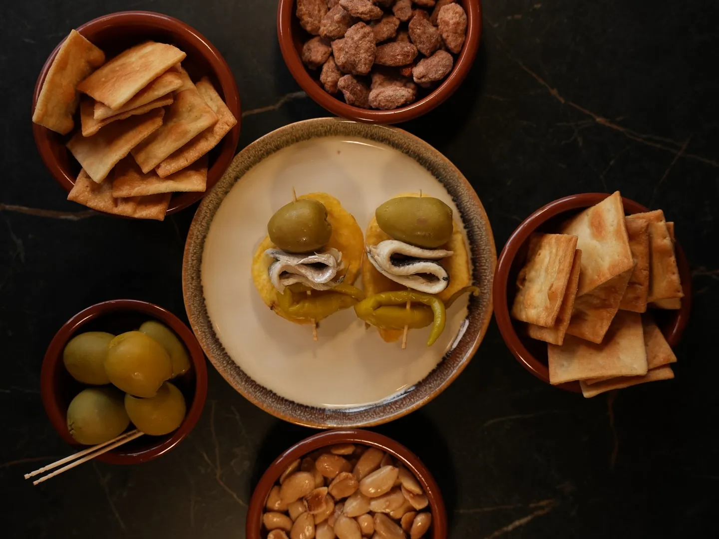 Olives, nuts, crackers and anchovy bites laid out for sharing