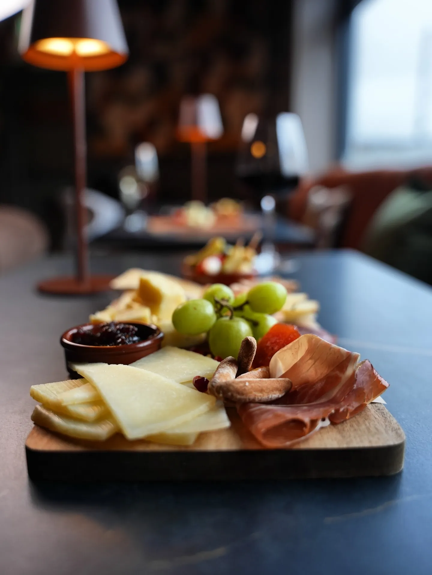 Cheese, cured meats, grapes and chutney on a board beside a table lamp