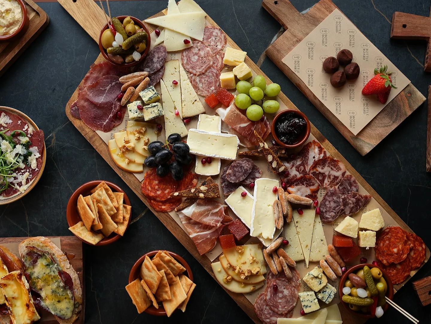 A spread of charcuterie, cheeses, grapes and crackers on wooden sharing boards